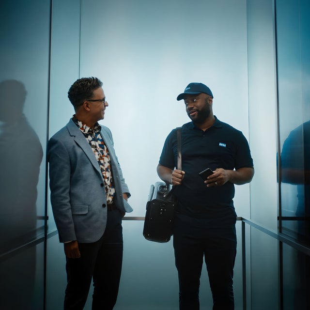 A KONE technician standing in an elevator shaft with a customer.