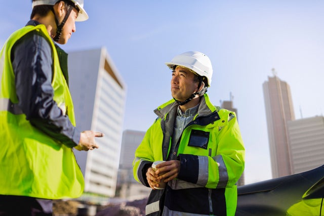 2 men on the construction site, talking, in helmets