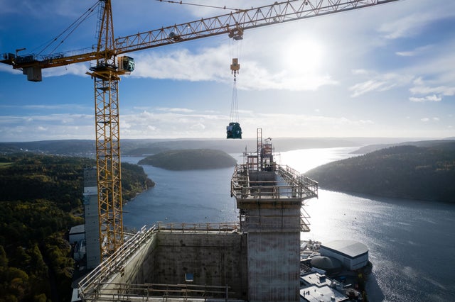 A building contruction site, a crane and a waterfront sceanery in the background