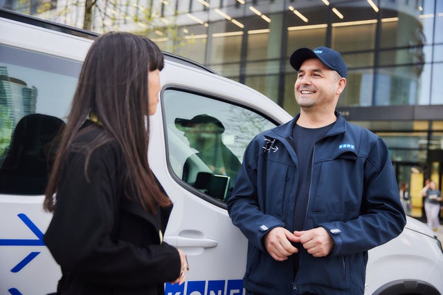 A KONE technician discussing with another person next to a KONE vehicle