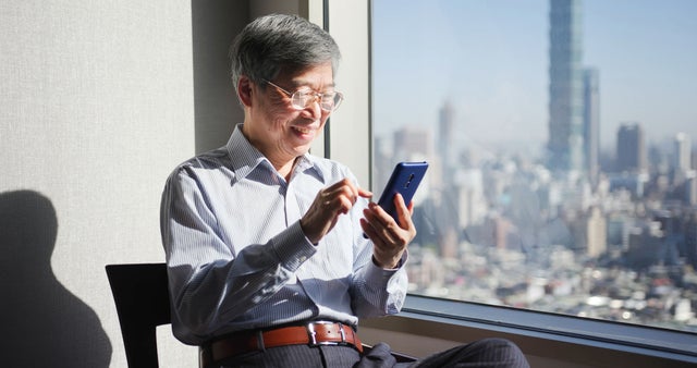 man looking at mobile phone with highrise view in window