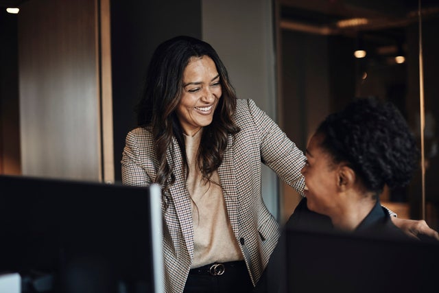 Two women talking and laughing near computer