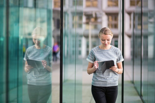 Young woman with tablet in front of glass building